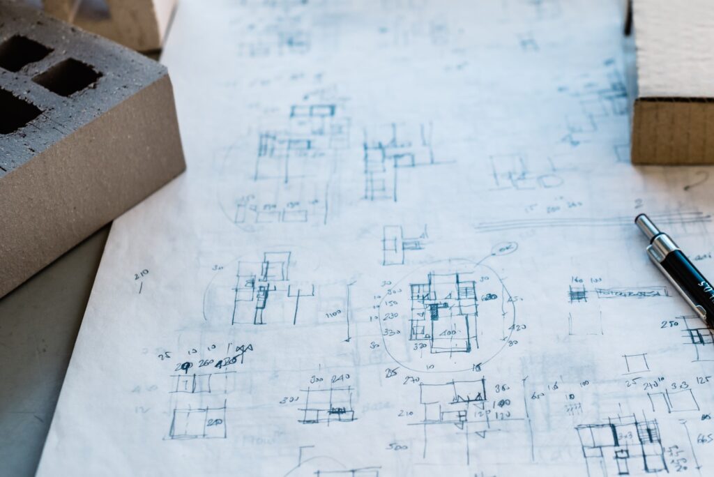 Desk with handdrawing sketches, pencil and brick blocks. Hand-drawn business detail sketch. Person is drawing a detail of a building or process on paper. Close up of pencil and notebook. Business process and strategy