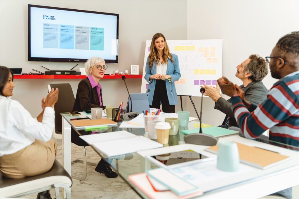 Business team in a meeting discussing strategy and planning. Professional group presentation led by a businesswoman. Corporate team collaboration in a modern office environment.